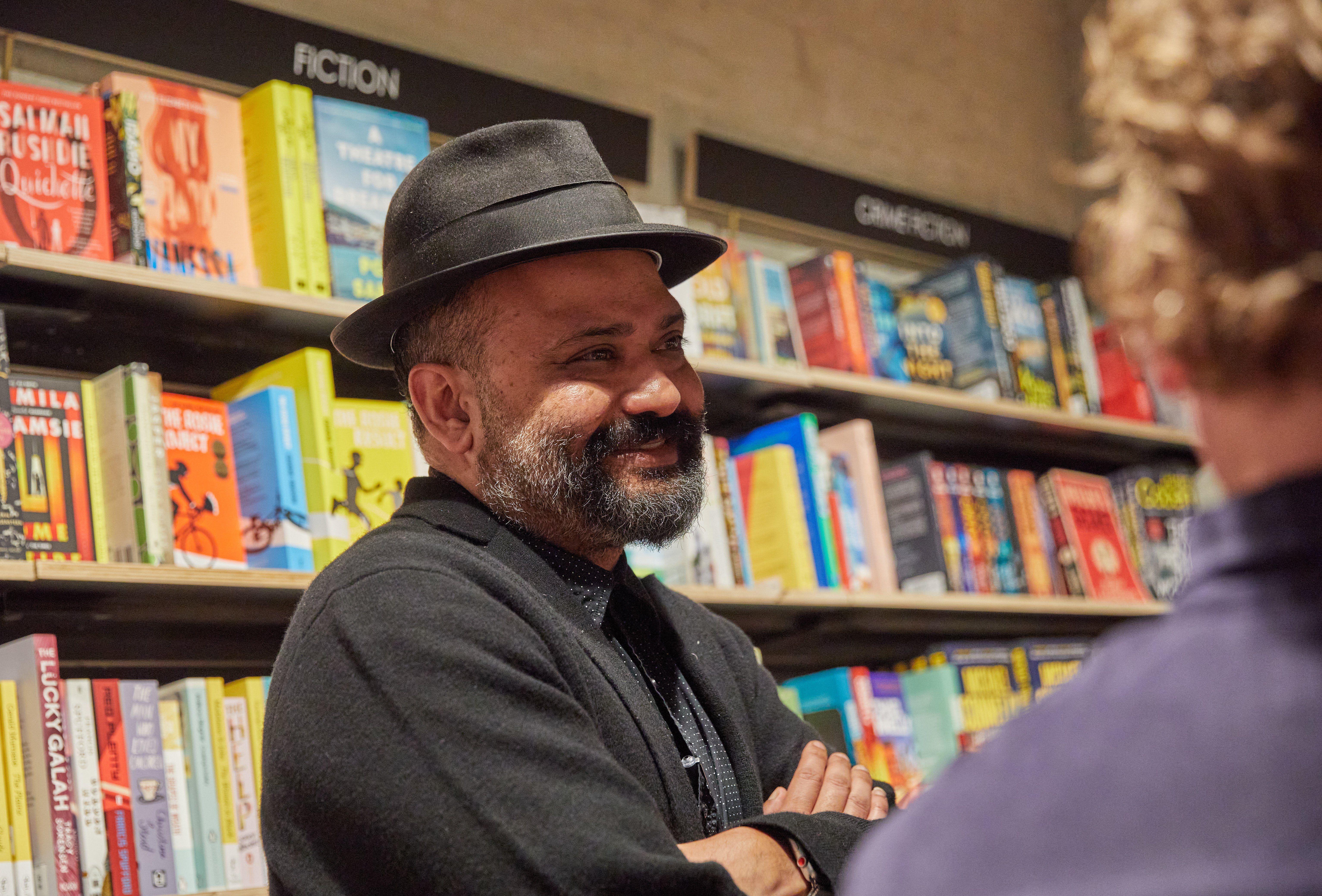 Man in hat with crossed arms talking to people in bookshop