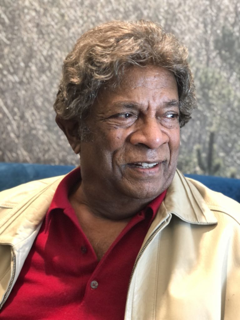 Photo of Australian-Malaysian singer Kamahl in red shirt and white jacket looking to the left