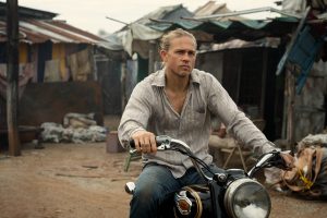 Actor Charlie Hunnam in loose white shirt on motorcycle with Bombay slum in background